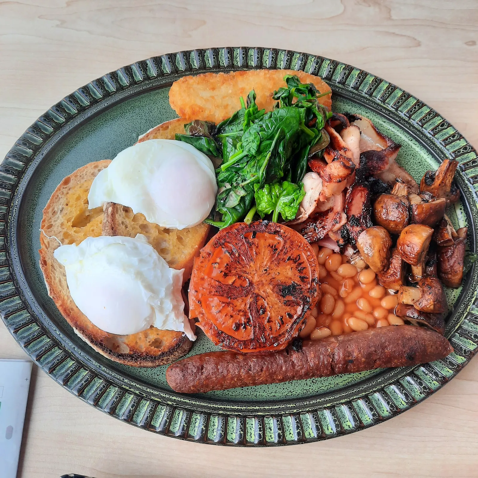 Full cooked breakfast on dark green ceramic plate with poached eggs, sourdough, beans and mushrooms