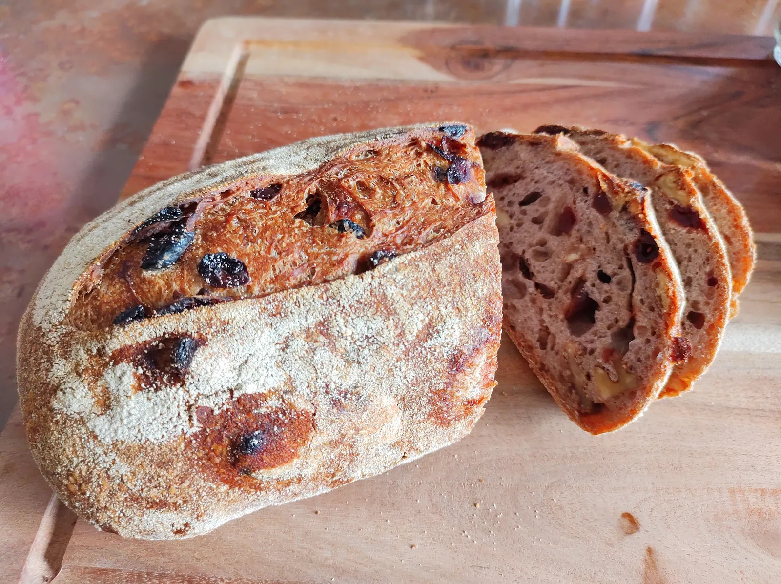 Sliced sourdough loaf with fruit inclusions on a wooden board
