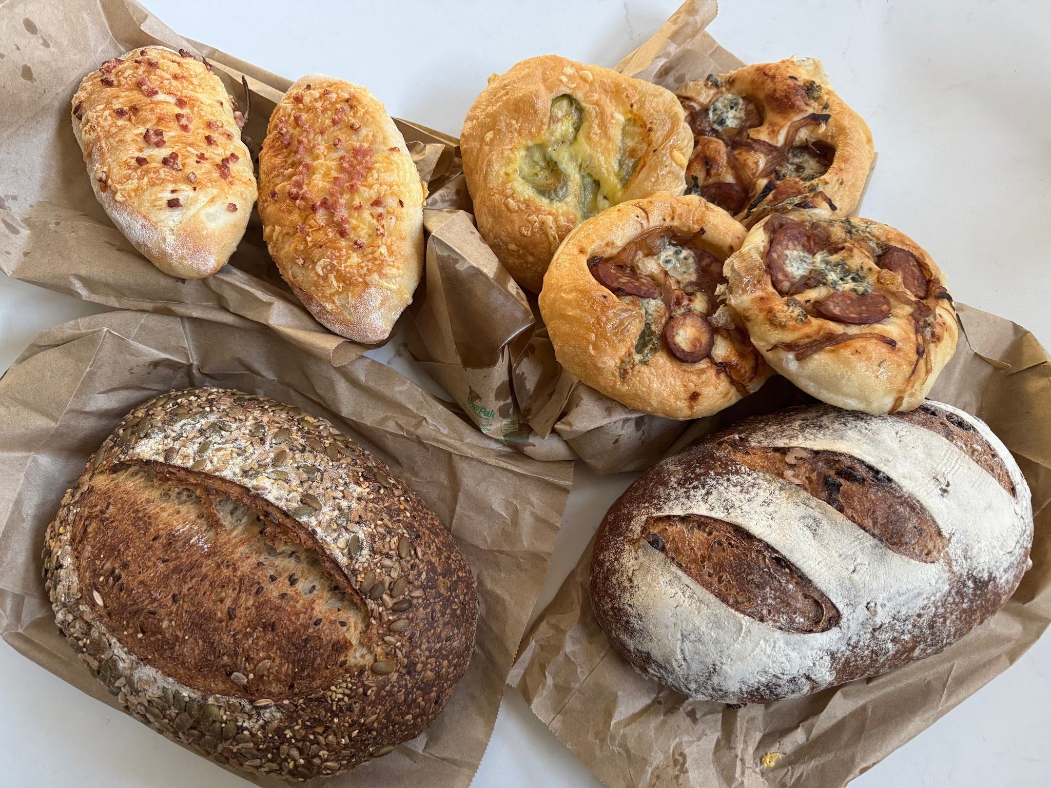Artisan bread assortment including sourdough boules and topped focaccia rolls on brown paper