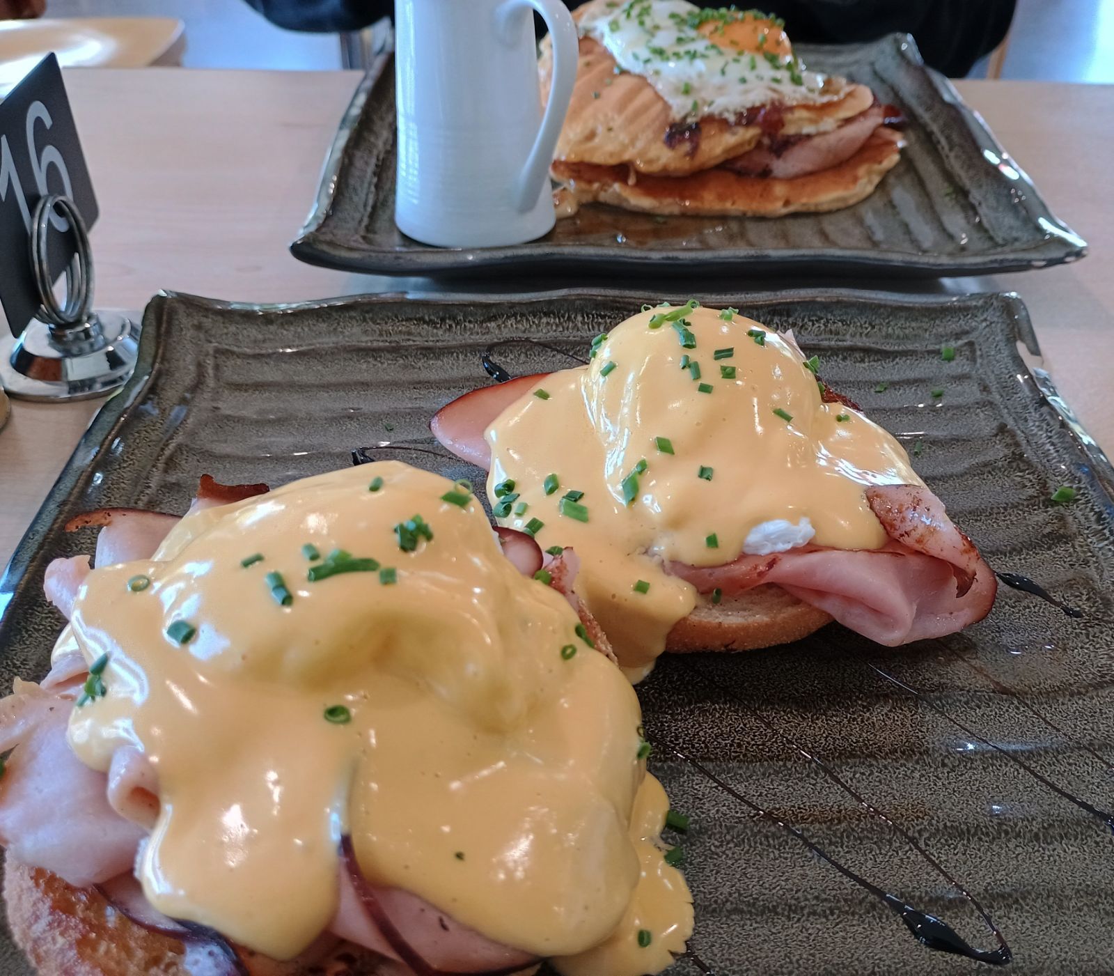 Eggs benedict with hollandaise sauce on waffle discs, dark ribbed ceramic plate