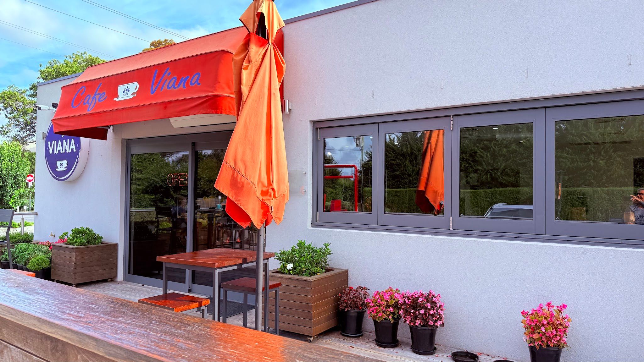 Cafe Viana exterior with red awning, outdoor seating and flowering planters in bright daylight