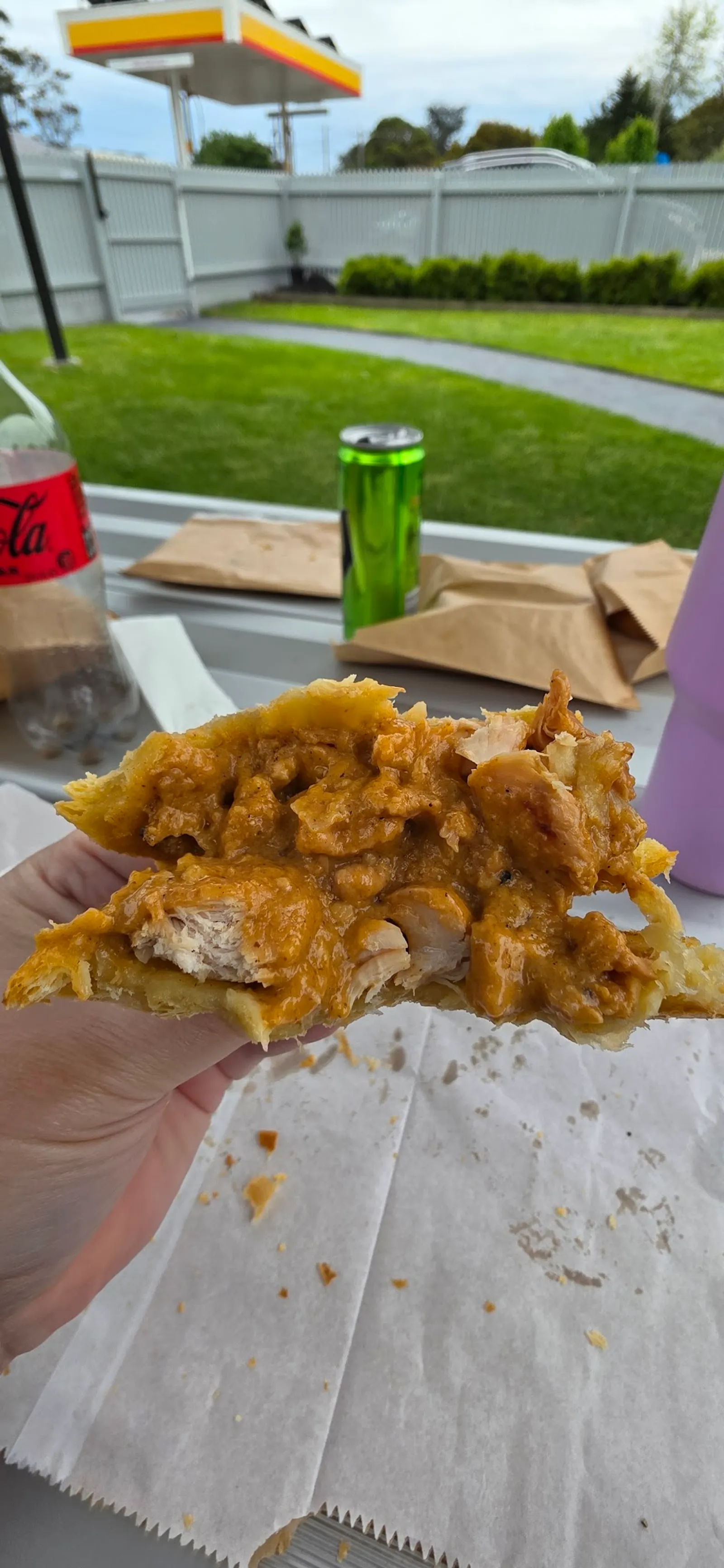 Hand holding open pastry pie with curried chicken filling, outdoor garden setting